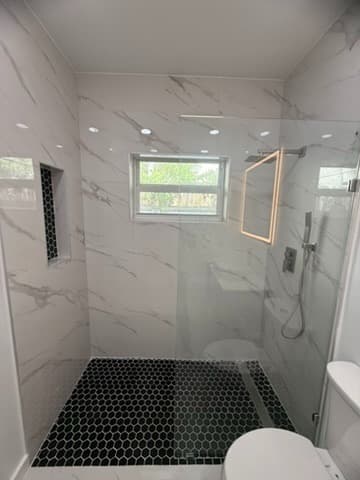 Overview of the finished walk-in shower with black hex tiles and linear drain.