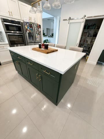 Detail view of the green island shaker drawers and gold pulls, complementing the warm floor and surrounding space.
