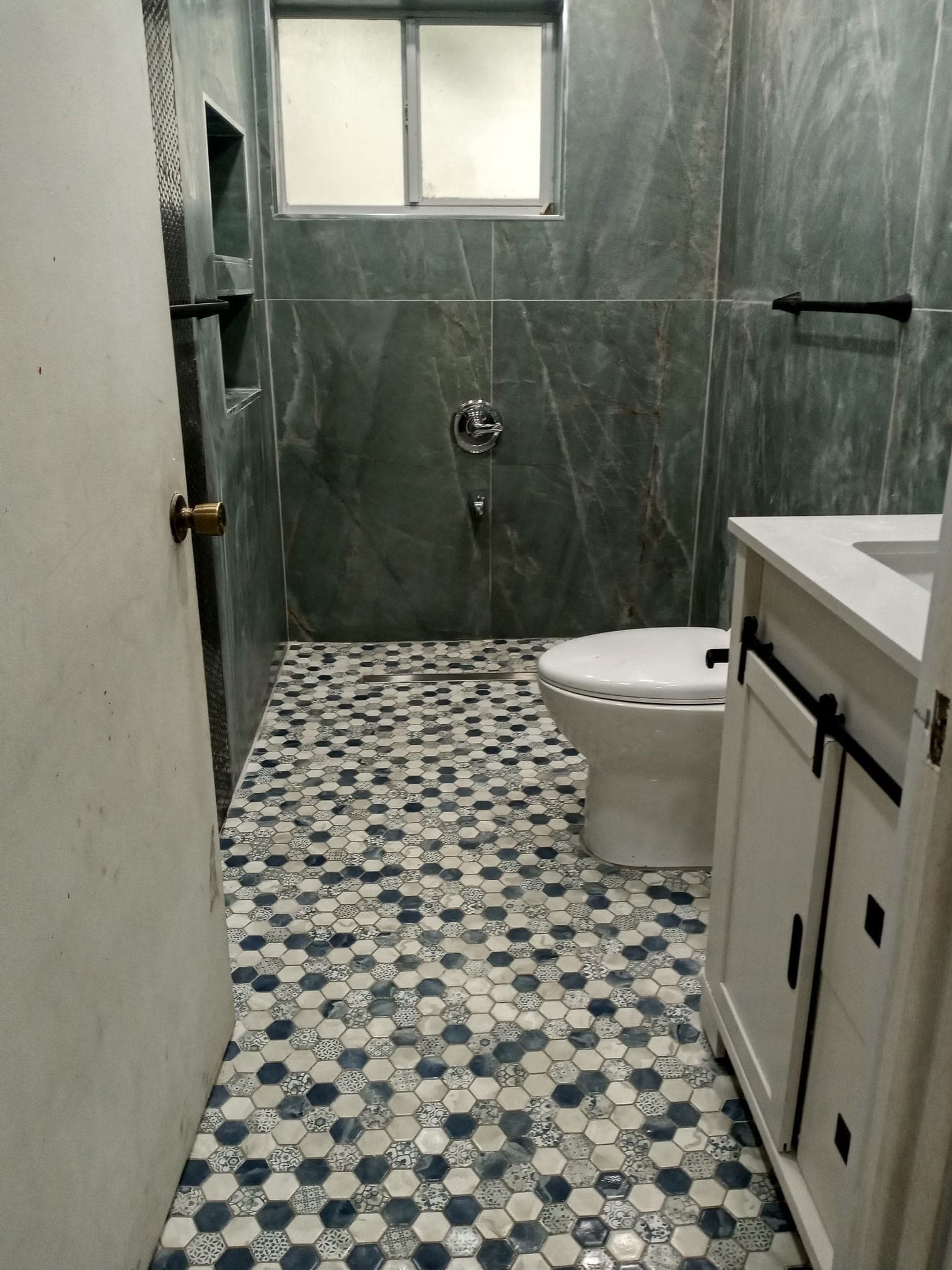 Tub to shower conversion in The Crossings with porcelain wall tile, a black hex shower floor and a tiled niche, photographed during installation