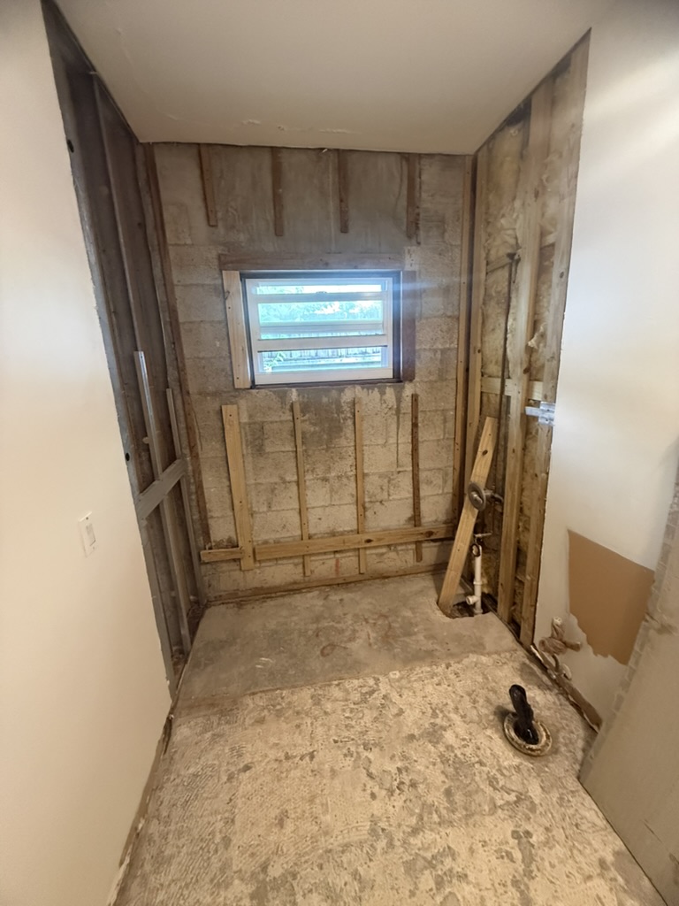 Bathroom wall opened after the tub was removed, exposing framing and the drain stub